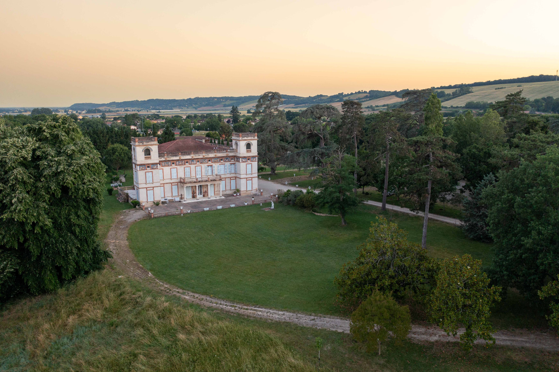 Aerial view of a grand estate at sunset, with manicured grounds and the sea beyond